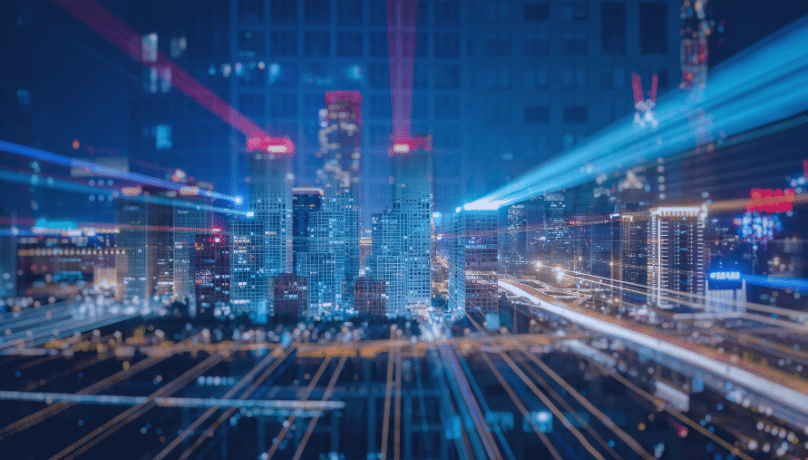 A vibrant city skyline at night, illuminated by lights and dynamic light trails from moving vehicles. 